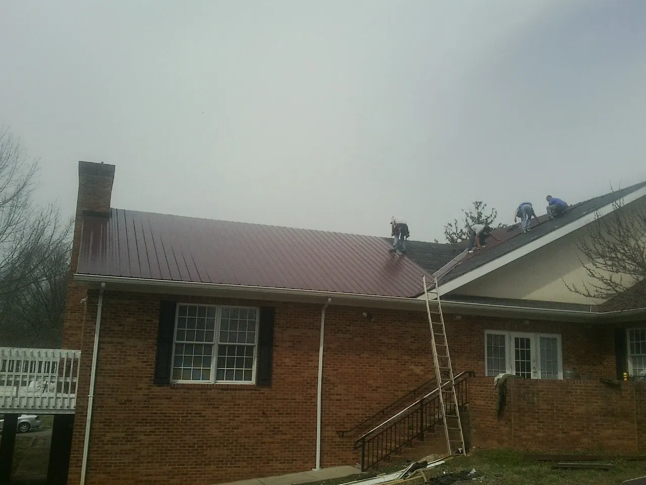 Crew setting red metal roofing panels on a brick home in Burlington
